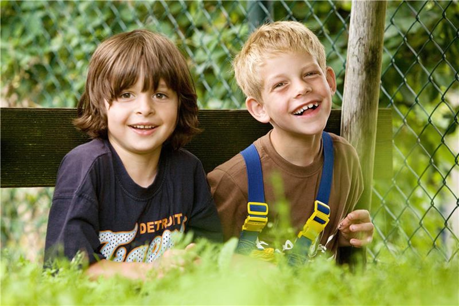 Zwei Jungen lachen in die Kamera. Sie sitzen im Gras und freuen sich des Lebens.